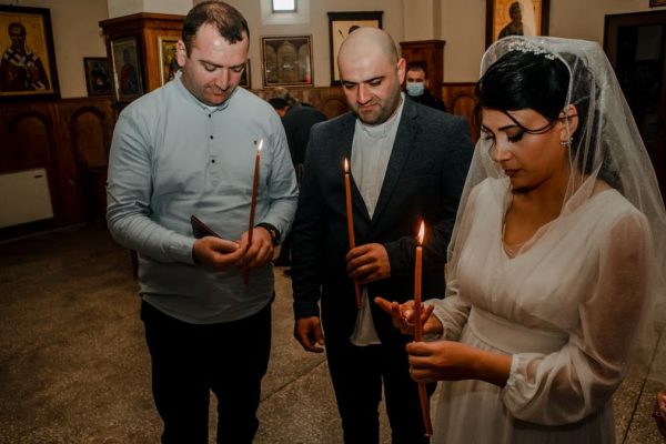 Bride and guests holding candles during an Orthodox wedding ceremony in a church setting.