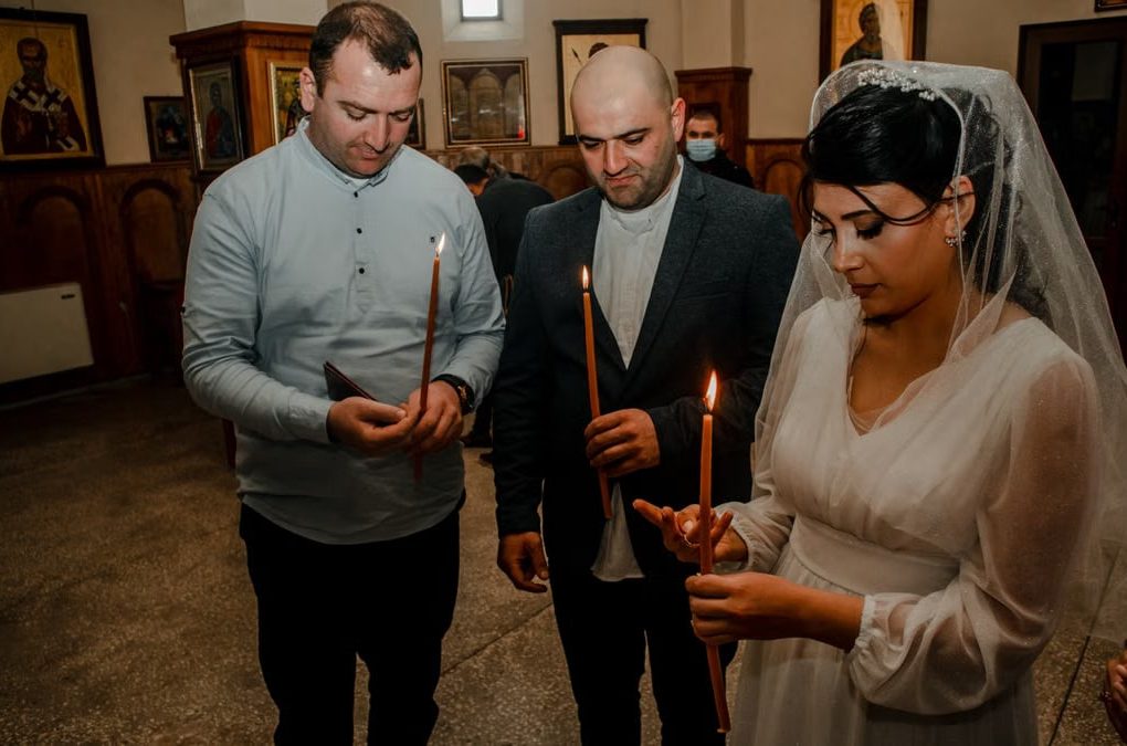 Bride and guests holding candles during an Orthodox wedding ceremony in a church setting.