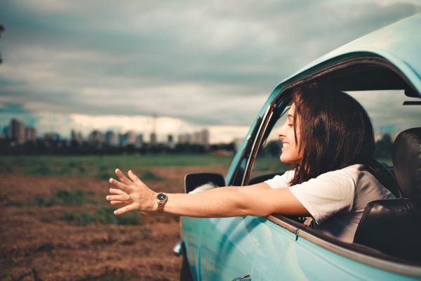Woman enjoying the fresh air while leaning out of a blue car window on a road trip.